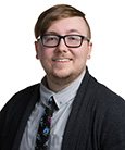 Headshot: Man with glasses in suit smiling at the camera.