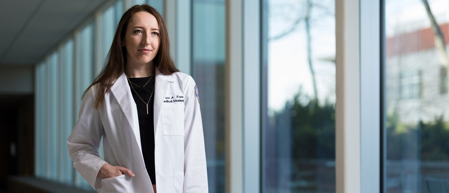 Student standing in O'Dowd Hall in her OUWB white coat