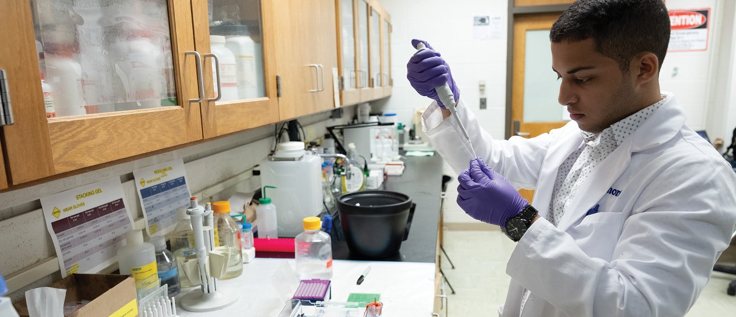 A man wearing a white lab coat, holding a medical syringe in a medical lab.