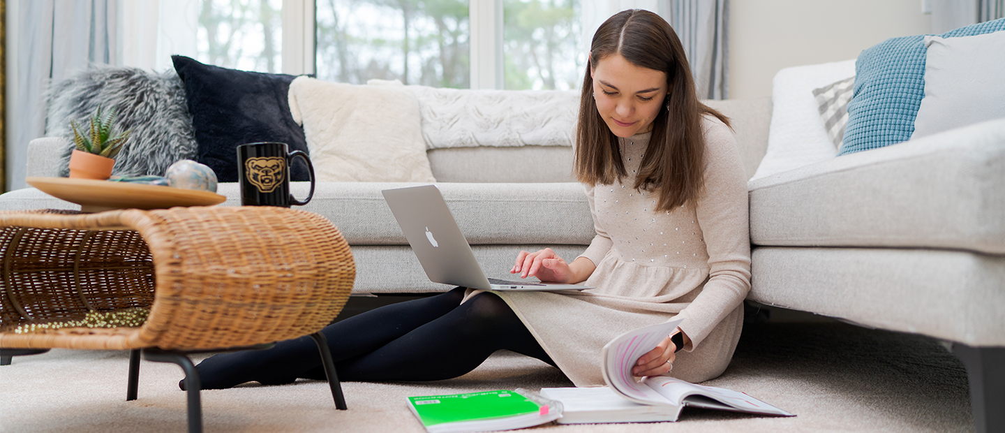 A student working on their computer sitting on the floor