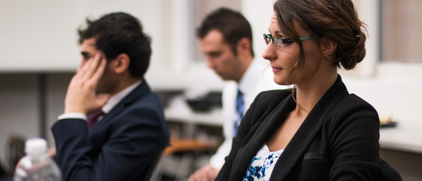 Three adults in business attire, seated at desks.