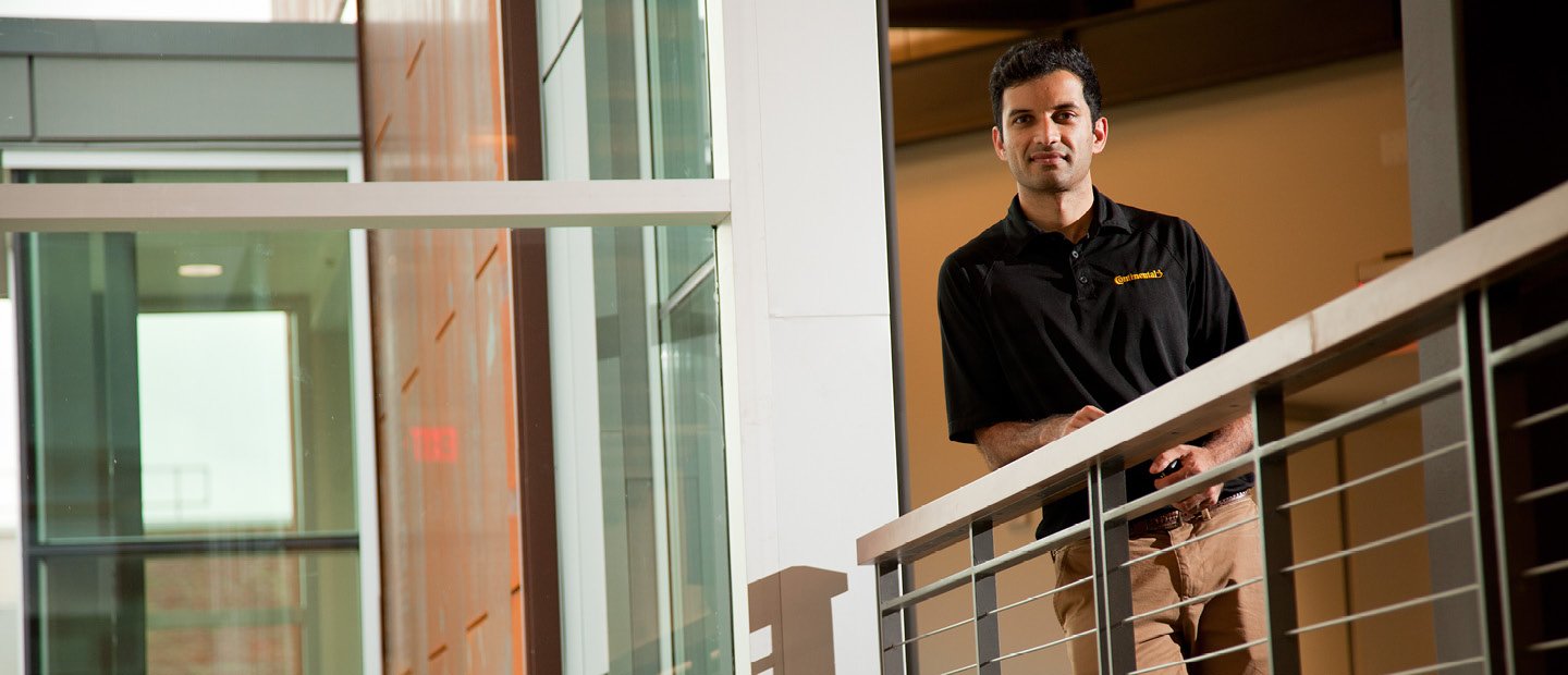 A man leaning on a railing in a hallway, looking down at the camera.