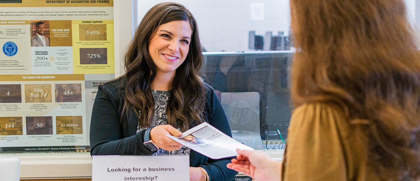 A woman standing in front of a graphic poster of statistics, handing a flyer to another person.