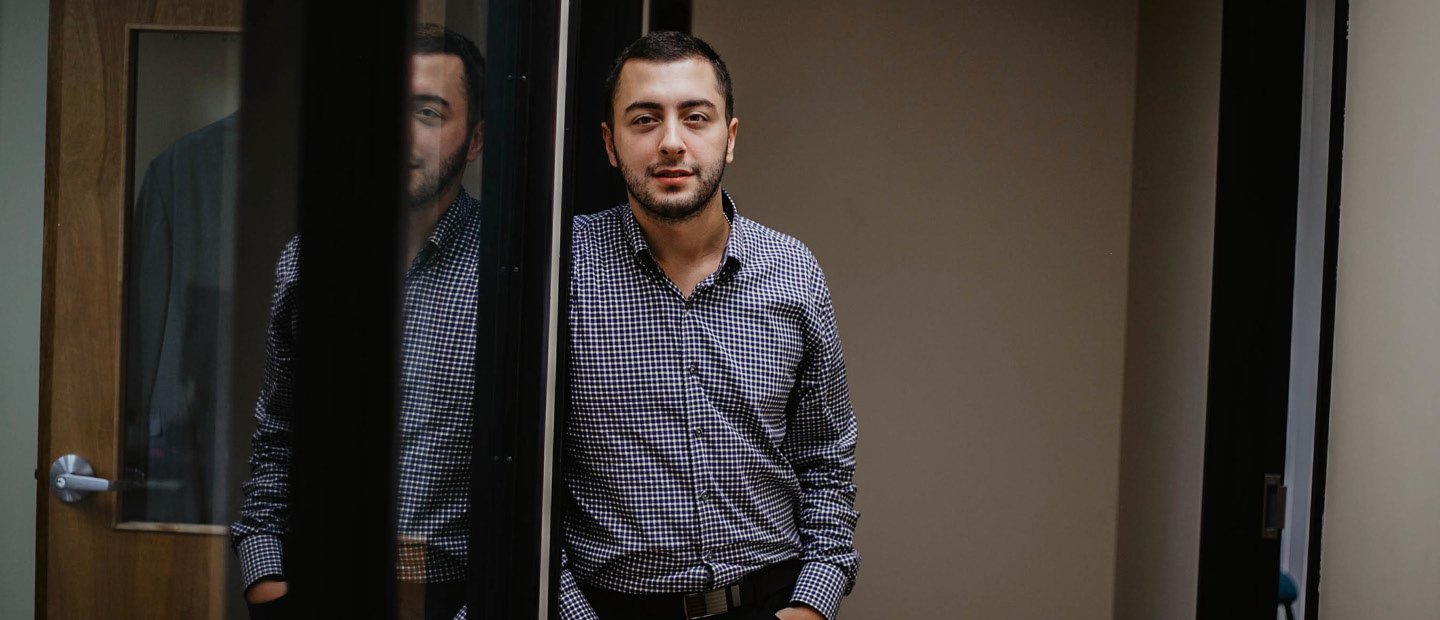 A young man looking at the camera, leaning against the side of an open doorway.