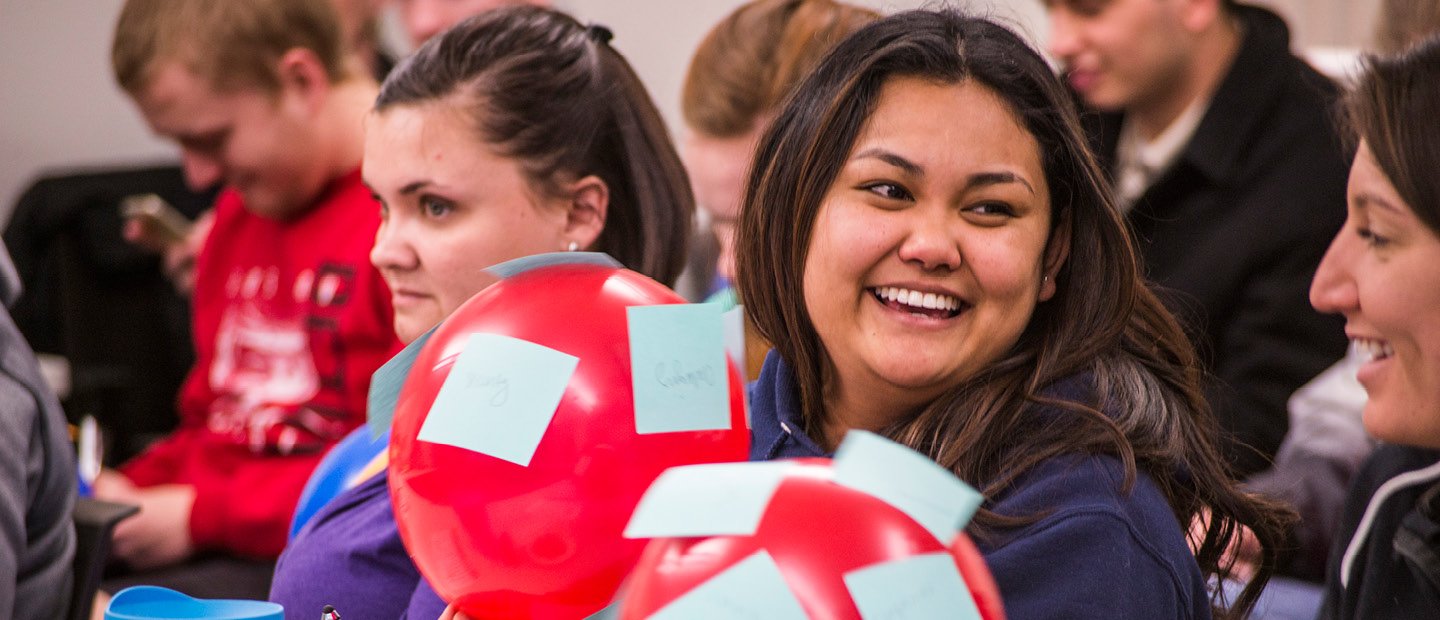 Students seated in a group, holding red balloons with blue sticky notes on them.