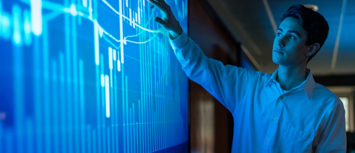 A young man pointing at a blue screen with a bar graph on it.