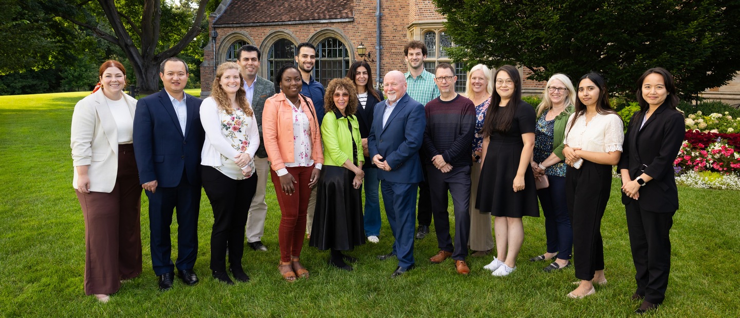 A group photo of Oakland University faculty standing outside of a large brick building.