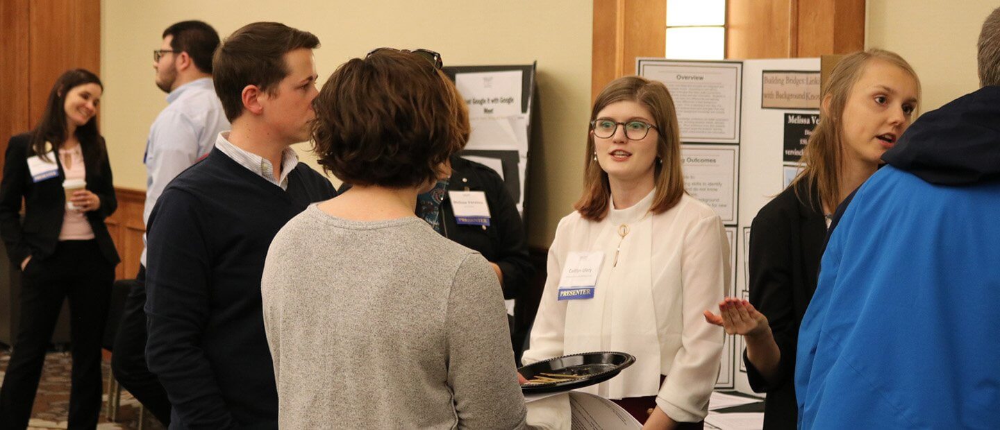 Adults in professional clothing viewing and discussing poster presentations in a conference room.