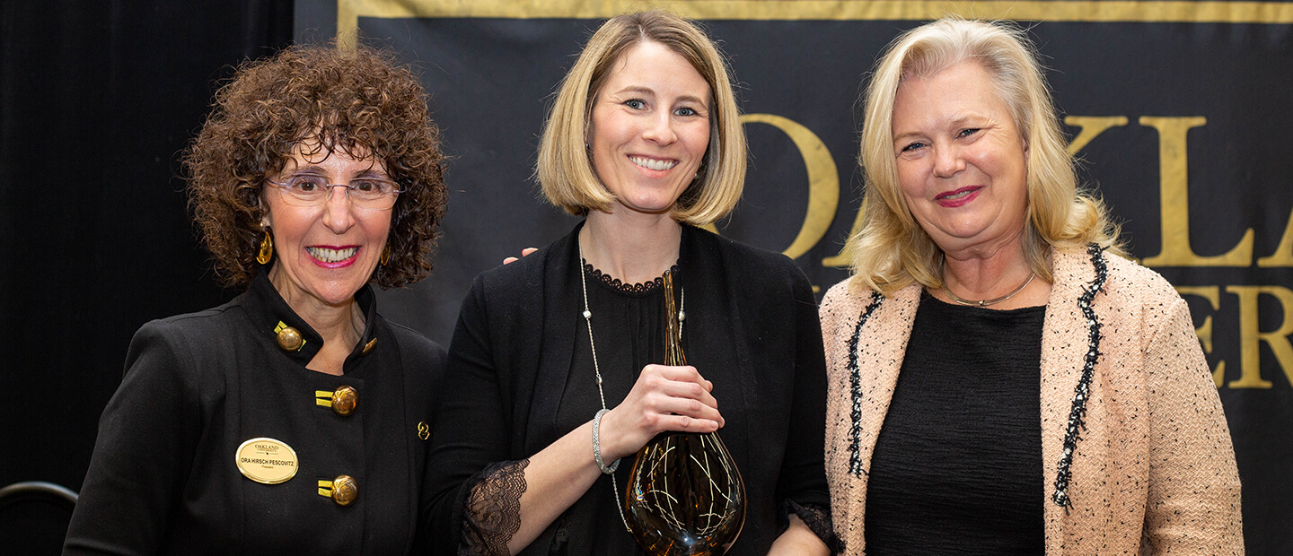 Three professionally-dressed adults smiling for a photo in front of a black backdrop.