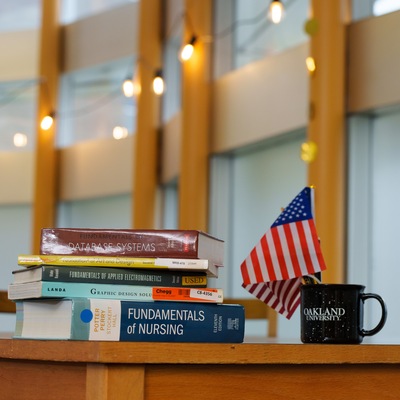 A stack of books and Oakland University on a desk.