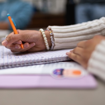 A closeup of a hand holding a pencil above a notebook.