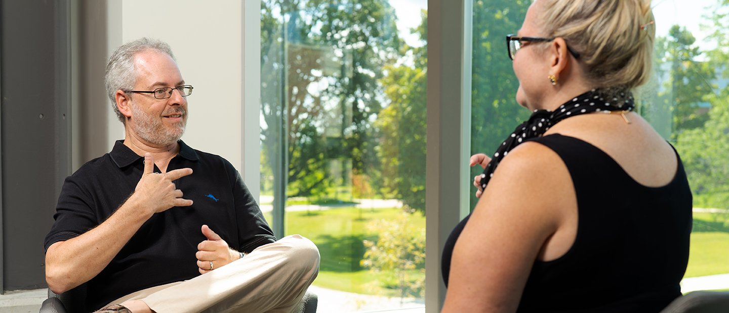 A man and a woman speaking to each other using American Sign Language.