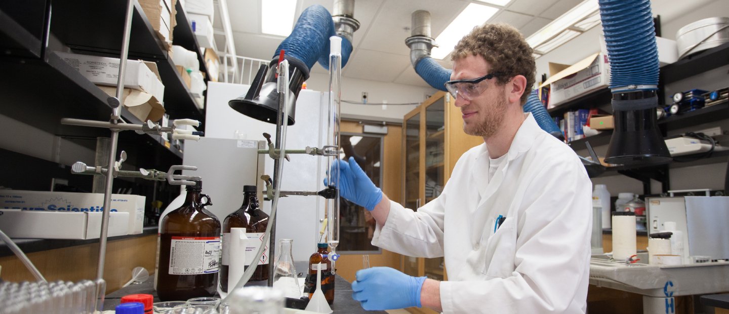 Man in goggles and lab coat works in a lab.