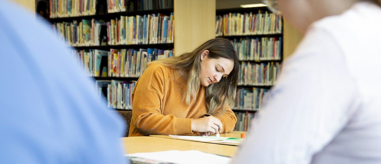 A woman takes notes on a pad of paper sittng at a desk in the Educational Resources Lab.