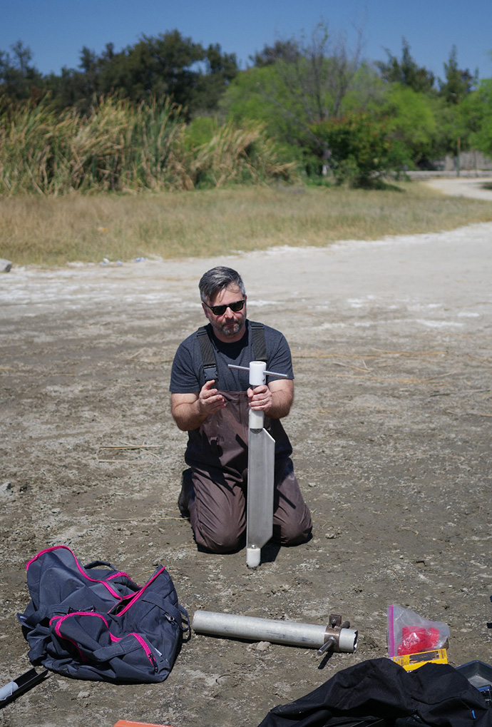Assistant Professor in the Department of Chemistry Thomas Bianchette digs in the ground in the field.