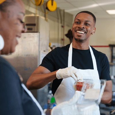 Man wearing an apron laughing with co-workers in a kitchen.