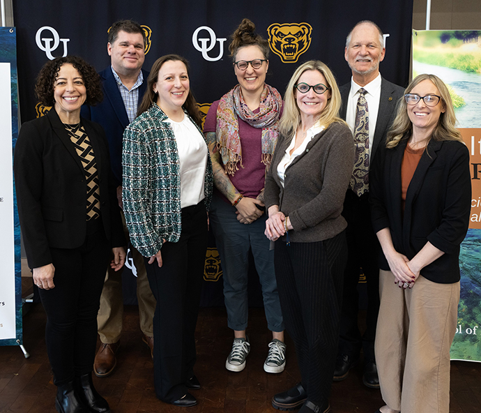 A group of people smiling in front of an OU background