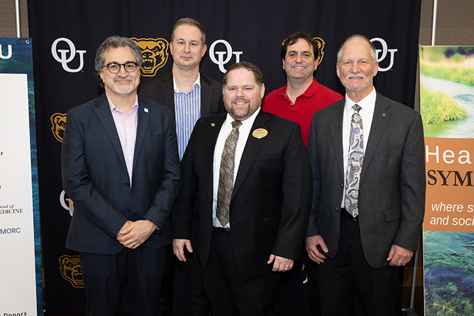A group of people smiling in front of an OU background