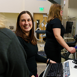 A woman smiles at someone off camera. Physical therapy equipment is behind her.