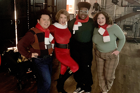 Four people wearing holiday clothes smile at the camera.