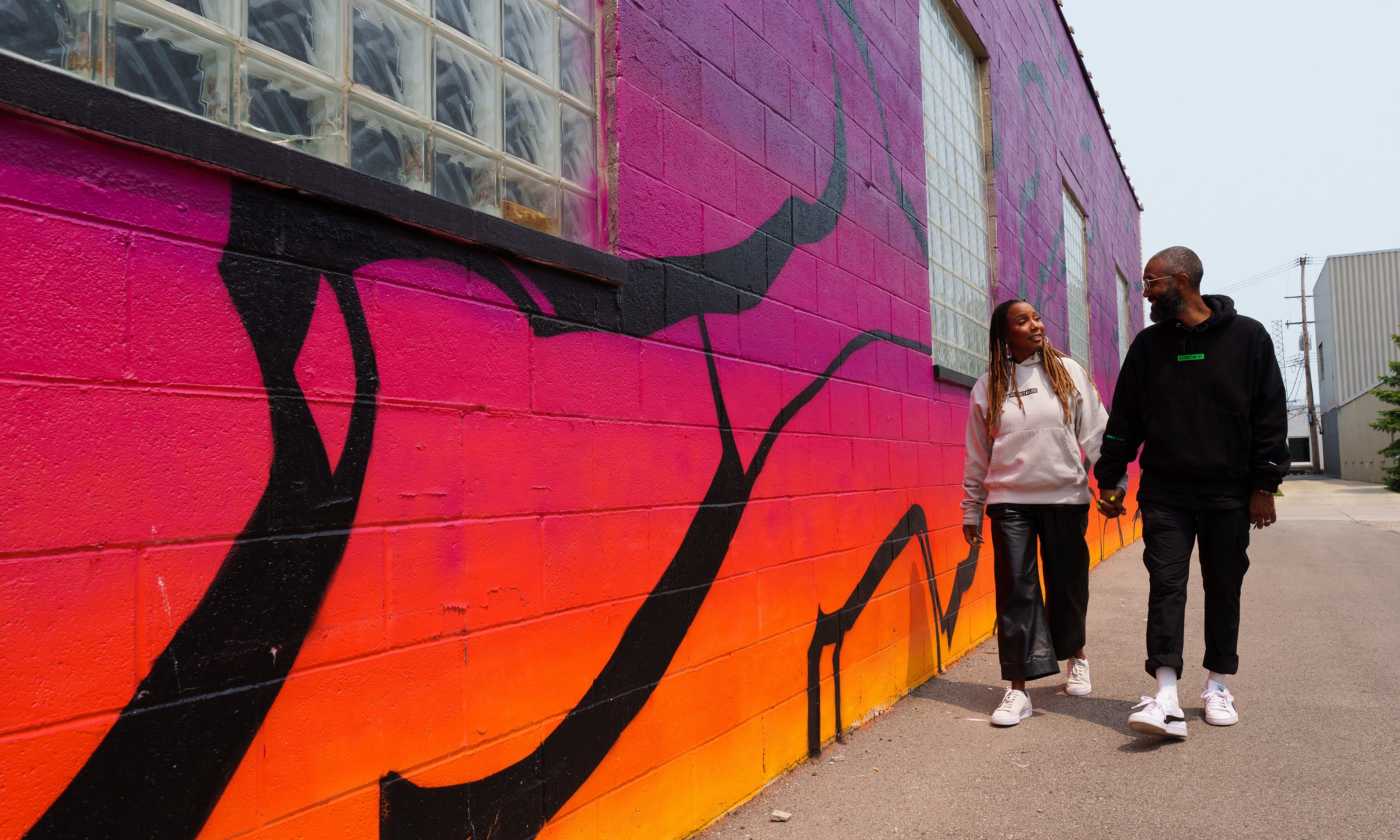 Two people walking outside next to a vibrant wall
