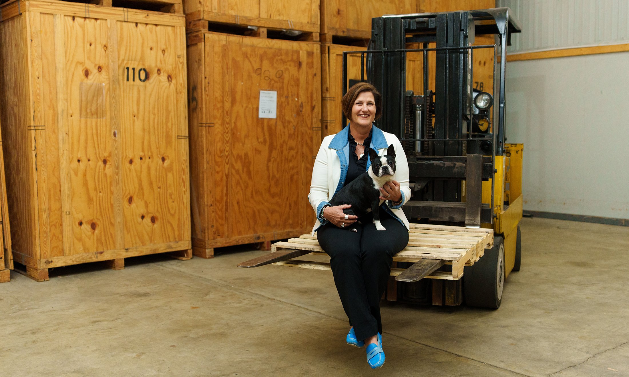 A woman holding a dog sitting while both sit on a forklift