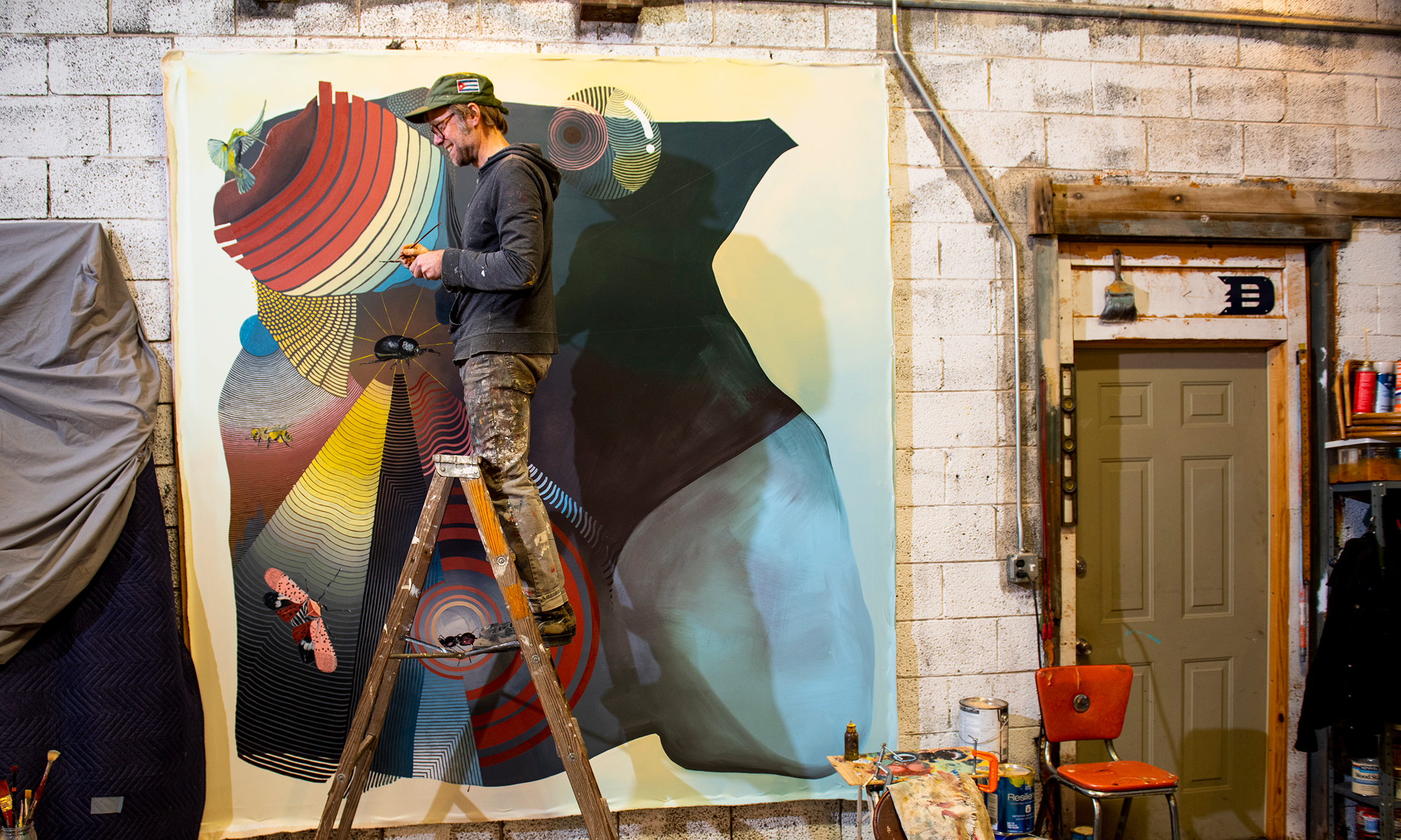 A man on a ladder painting a mural