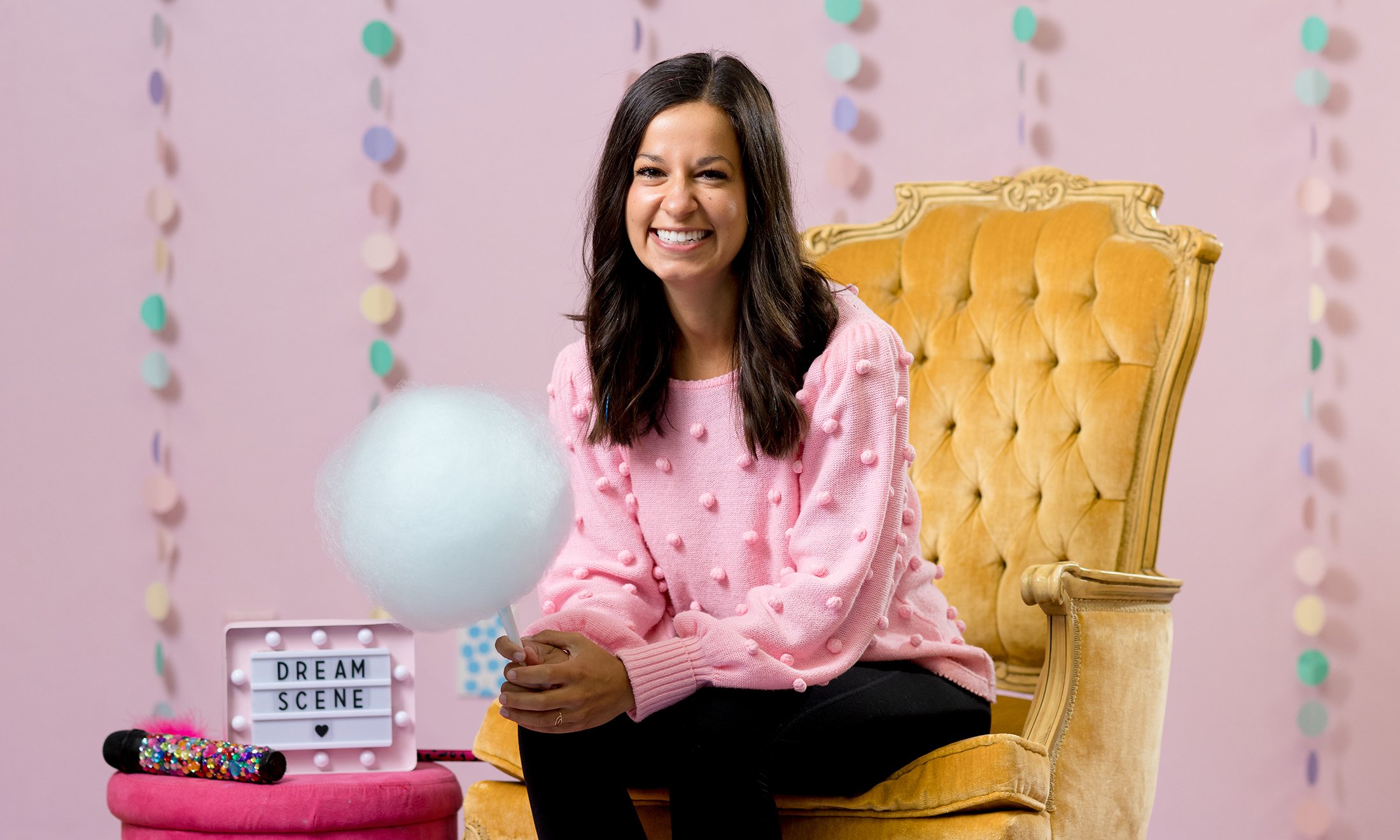 A woman in a chair holding cotton candy, to her right is a sign that reads, 