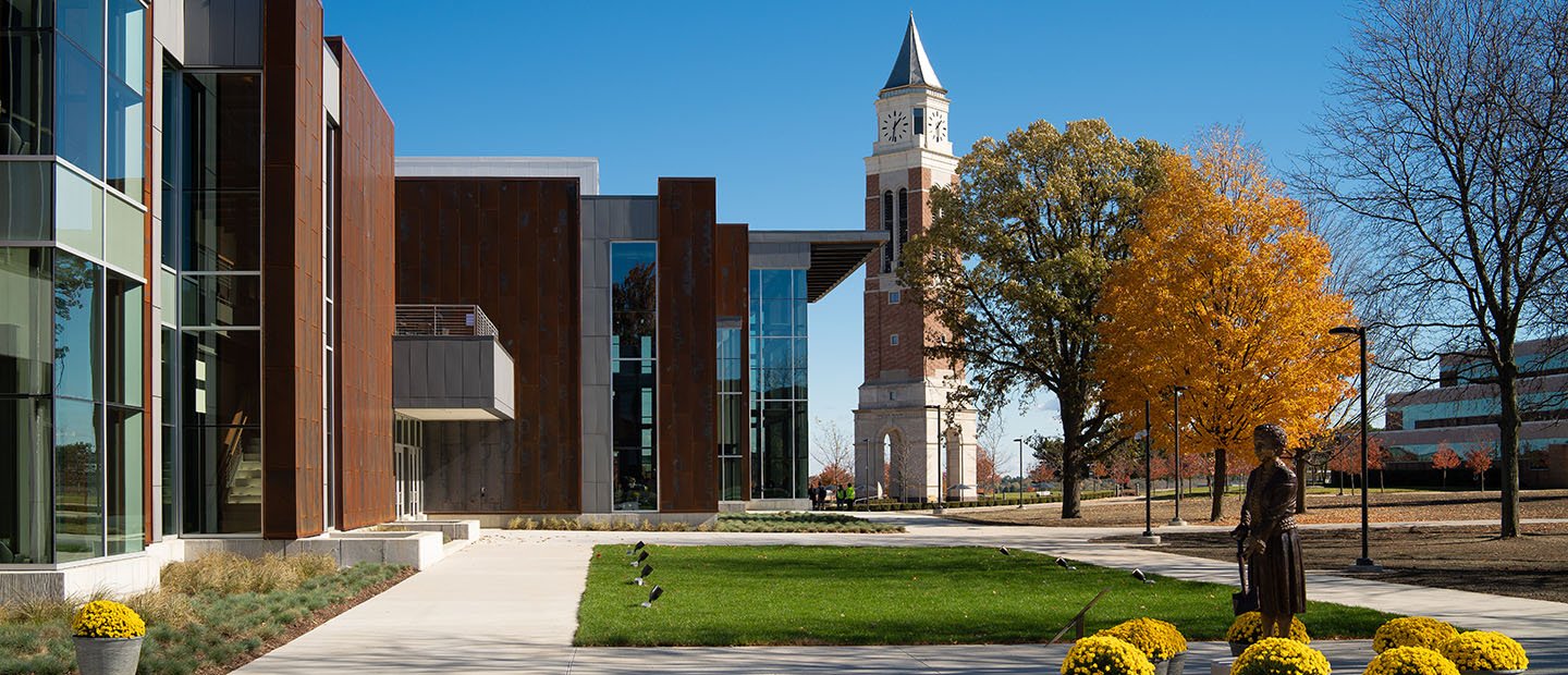 exterior of a brown building with a lot of windows, clock tower in the background