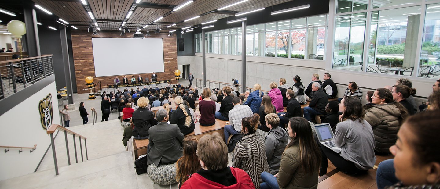 panel of people seated in front of a large white screen, facing an audience