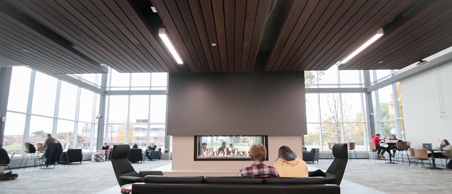 People seated on a couch looking towards a fireplace in the center of a large room.