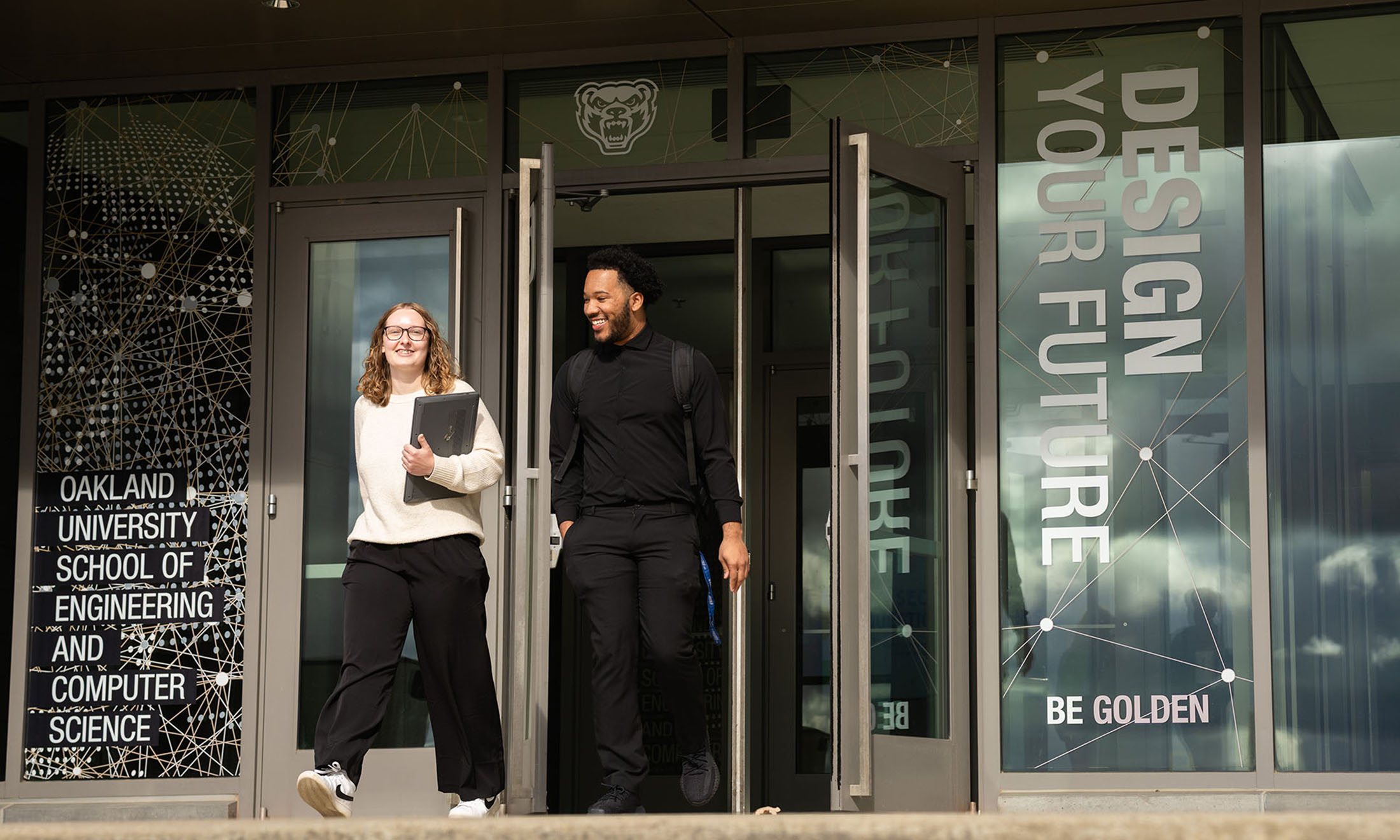 Two students walking out of the building; the sign says Design Your Future