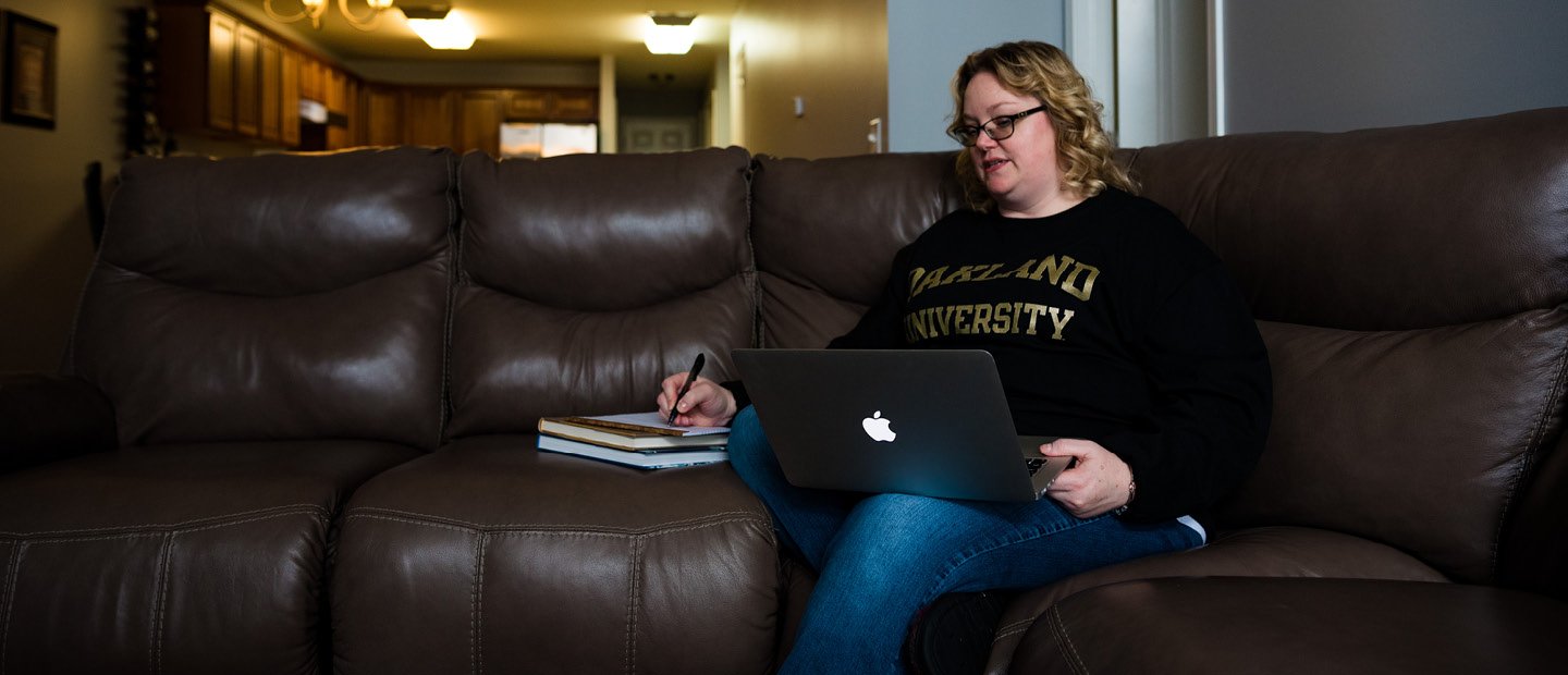 A woman sits on a living room sofa with her laptop open.