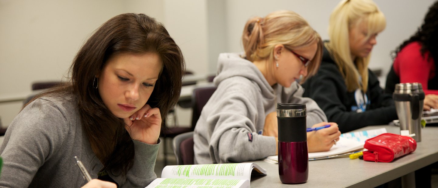 Students seated at a long desk, taking notes.