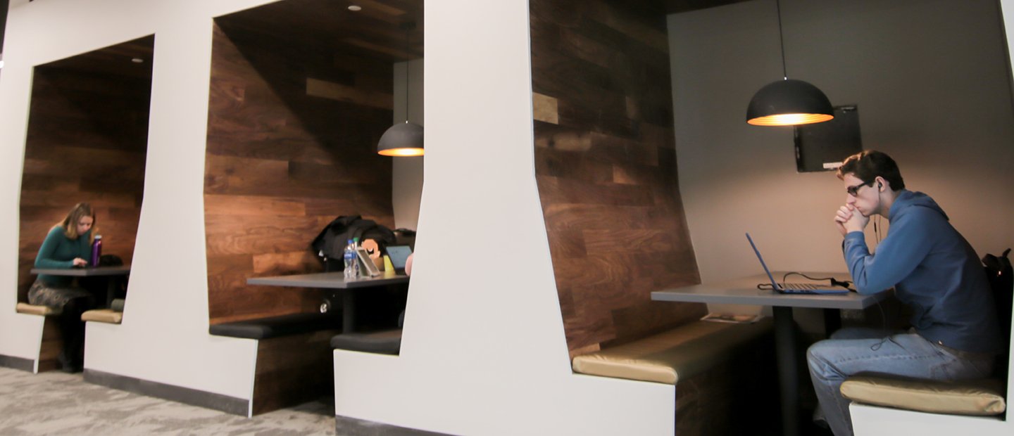 Students sitting at benches set into the wall in a common space at Oakland University.