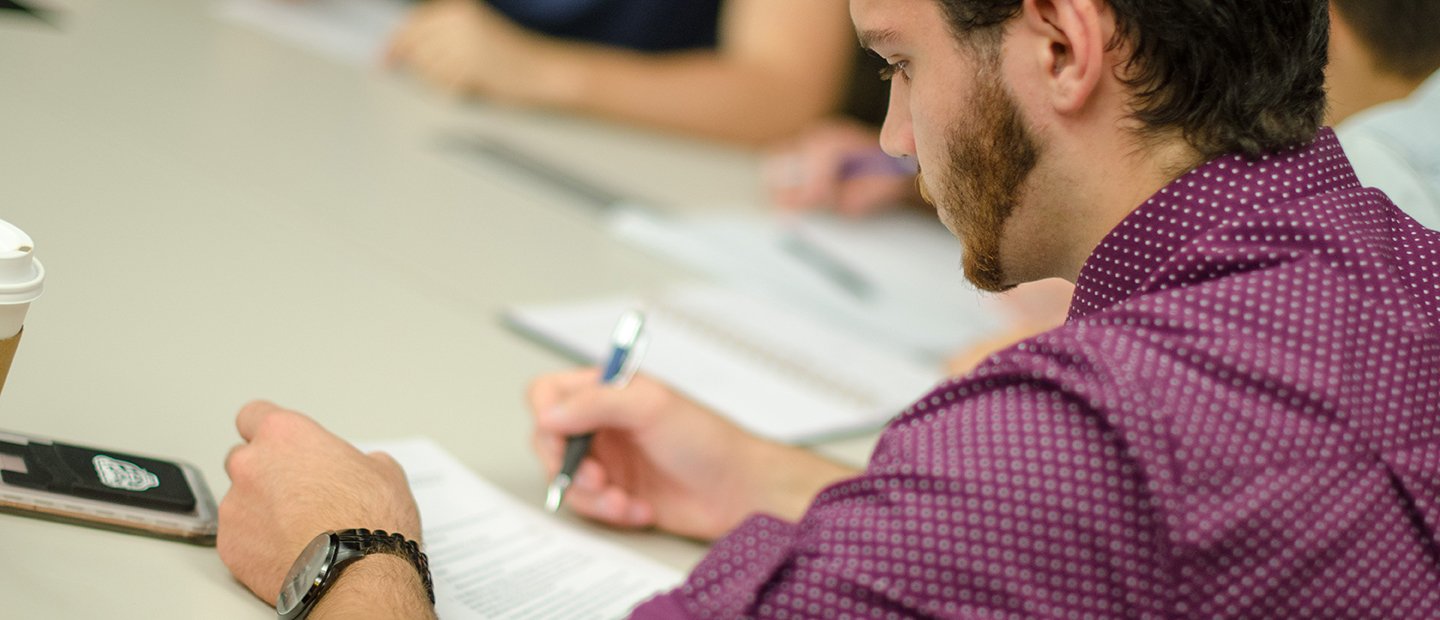 A young man seated at a table, filling out a document.