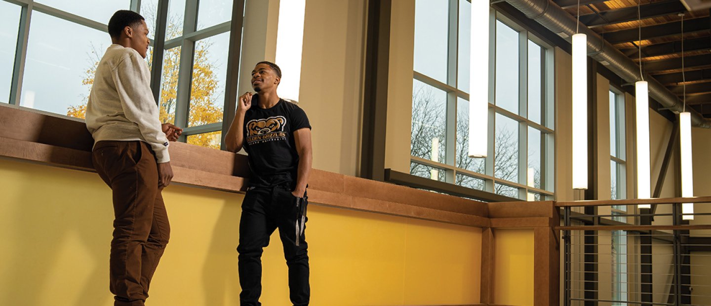 Two young men leaning on a window sill, talking.