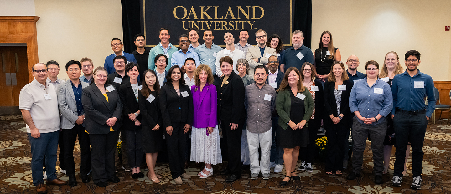 A group photo of Oakland University faculty standing inside in front of the Oakland university logo.