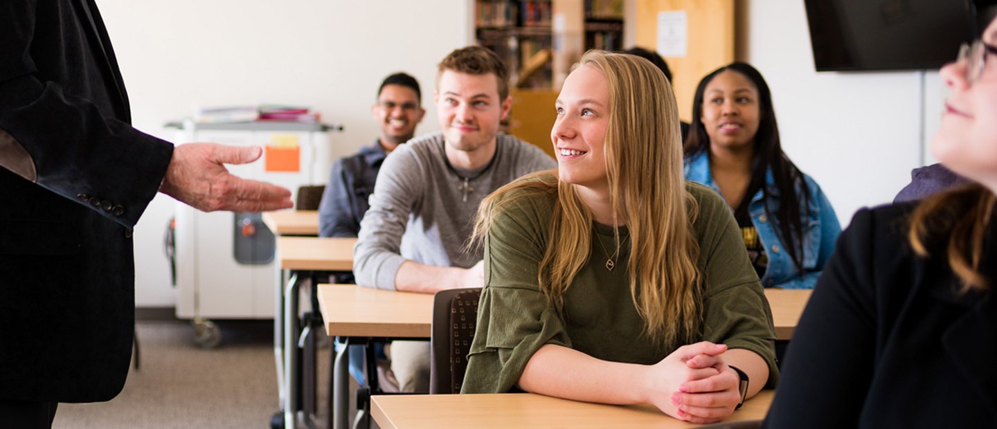 classroom full of students watching a professor who is gesturing with his hands