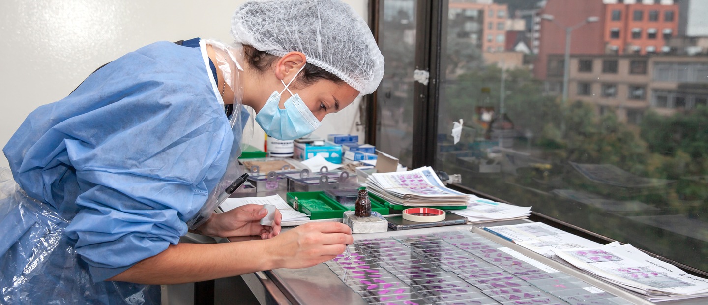 A woman holding up a slide while another woman looks into a microscope