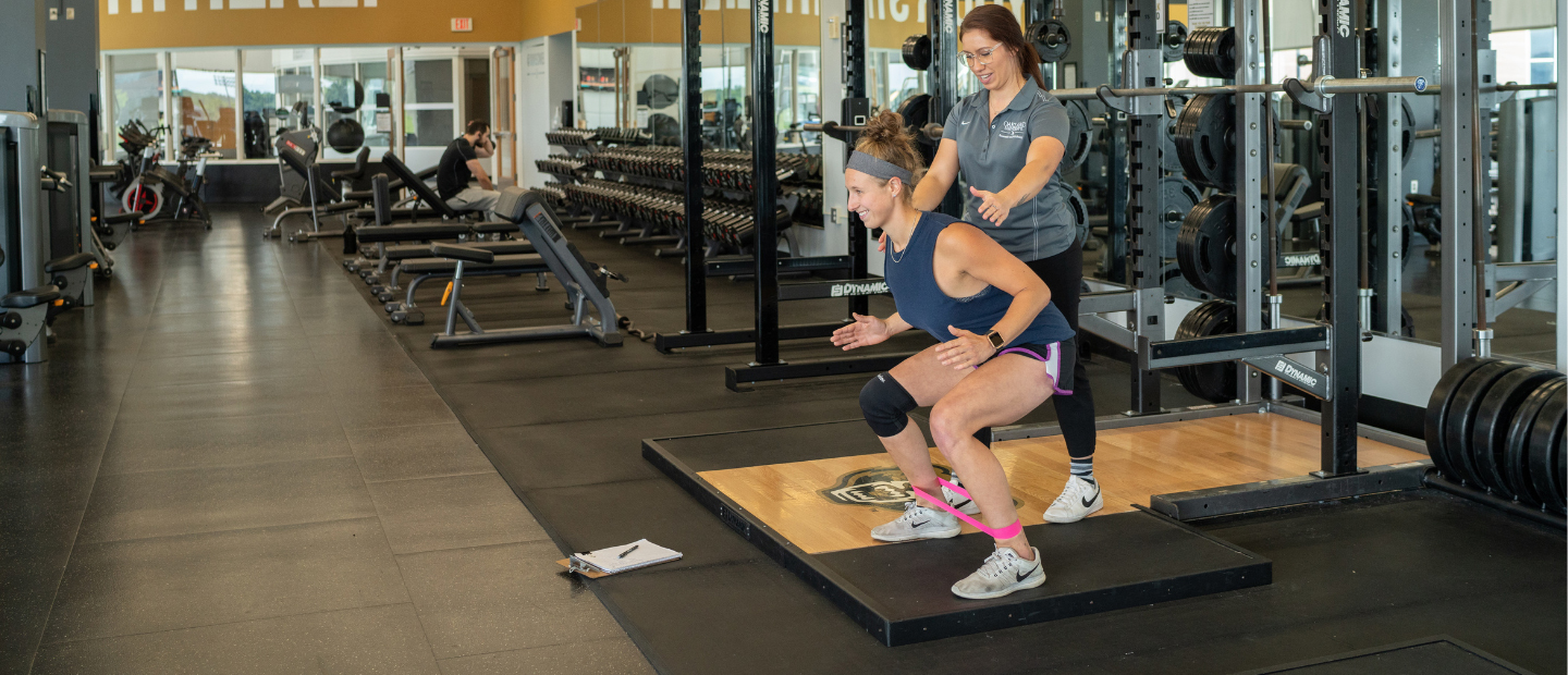 A personal trainer guiding a client in a squat.