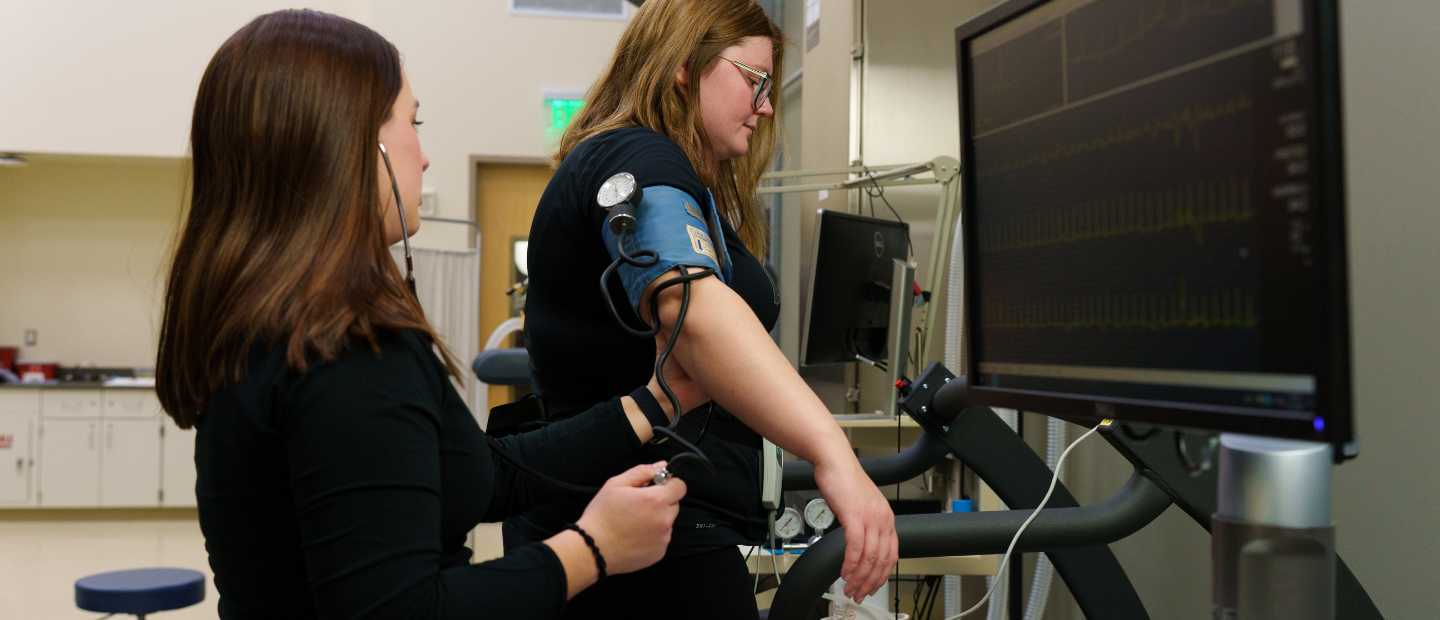 A woman taking another woman's blood pressure on a treadmill.