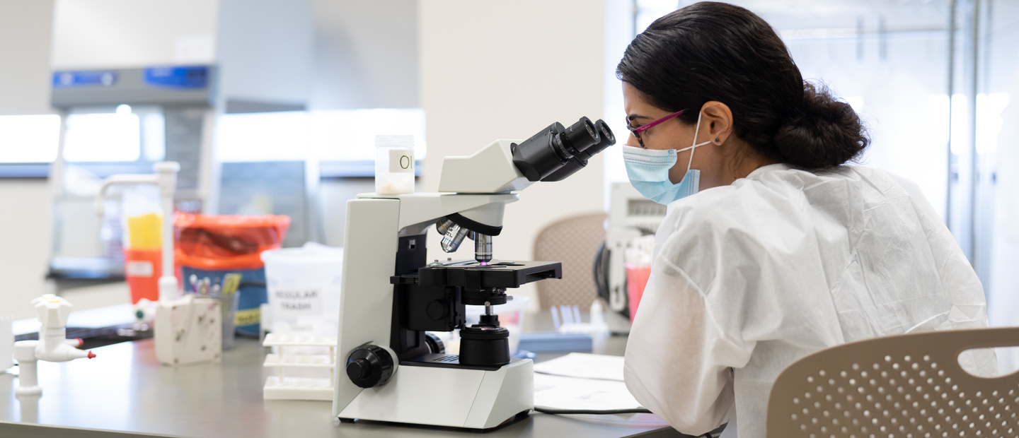 A woman in a lab looking into a microscope.