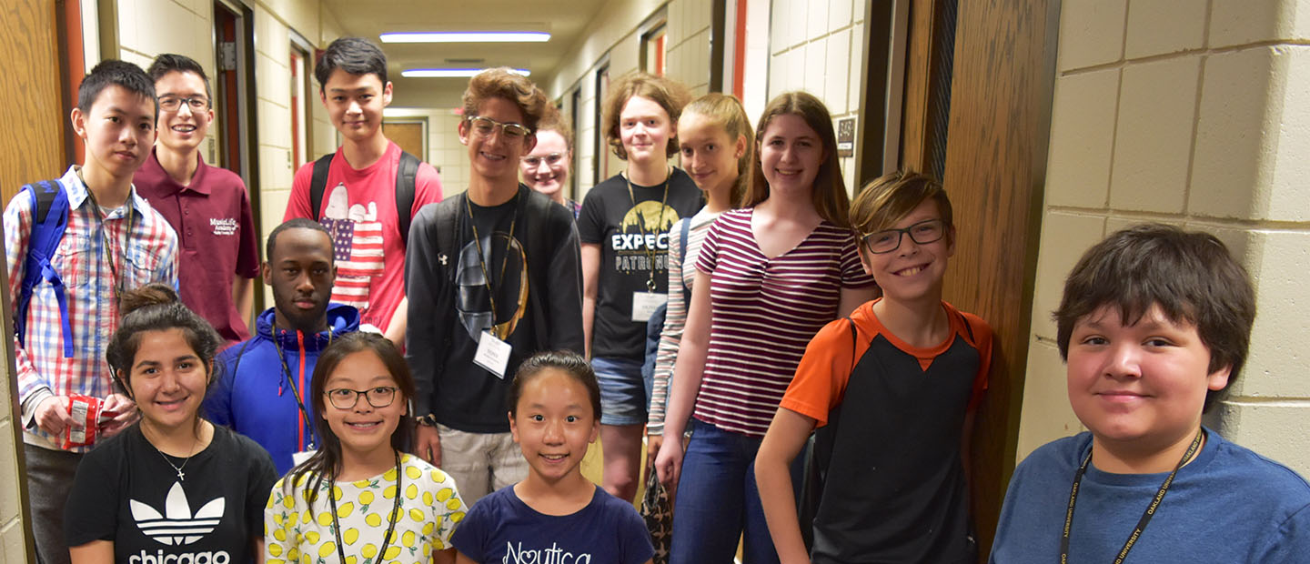 A group of children stand in an Oakland University building smiling at the camera.