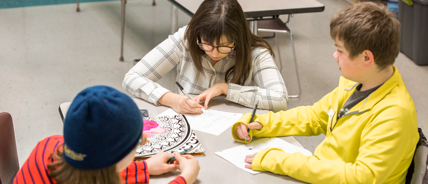 An aerial photo of three kids seated at a table, writing.