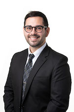 Shane Lewis posing for a professional headshot wearing a black suit and tie