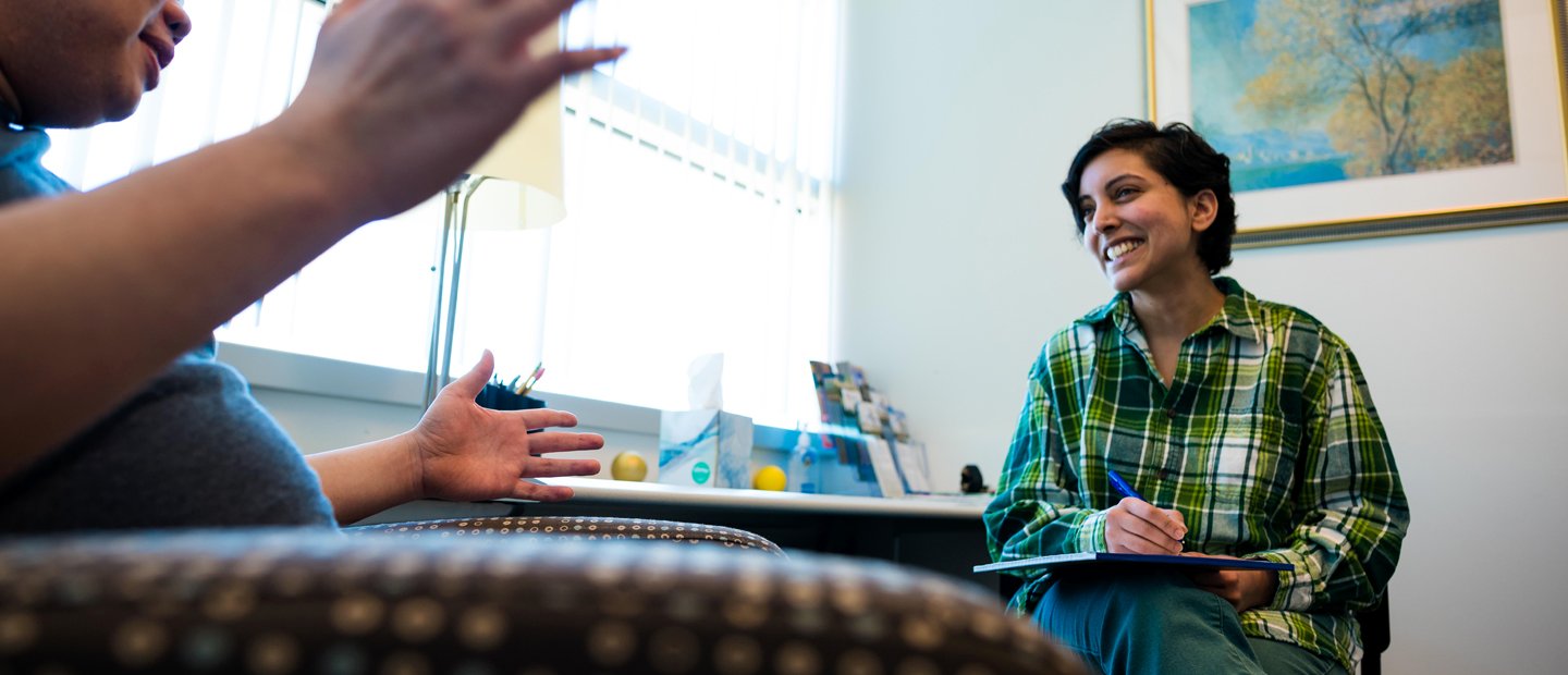 Two people seated in an office, facing each other, smiling and talking.