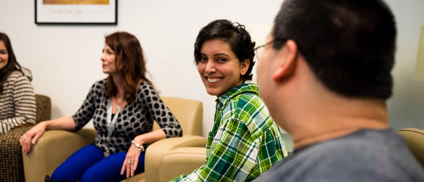 Four people seated in a row of arm chairs, smiling.