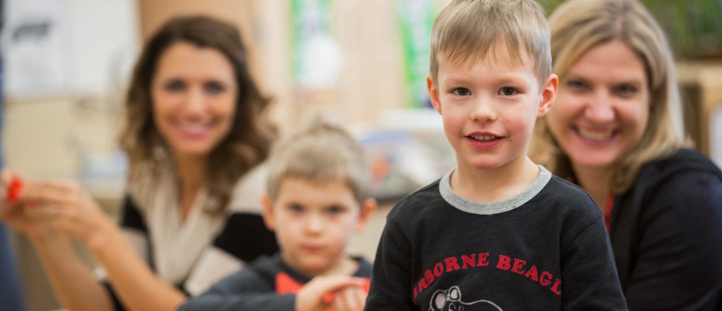 kid looking at the camera with two women and one other kid in the background