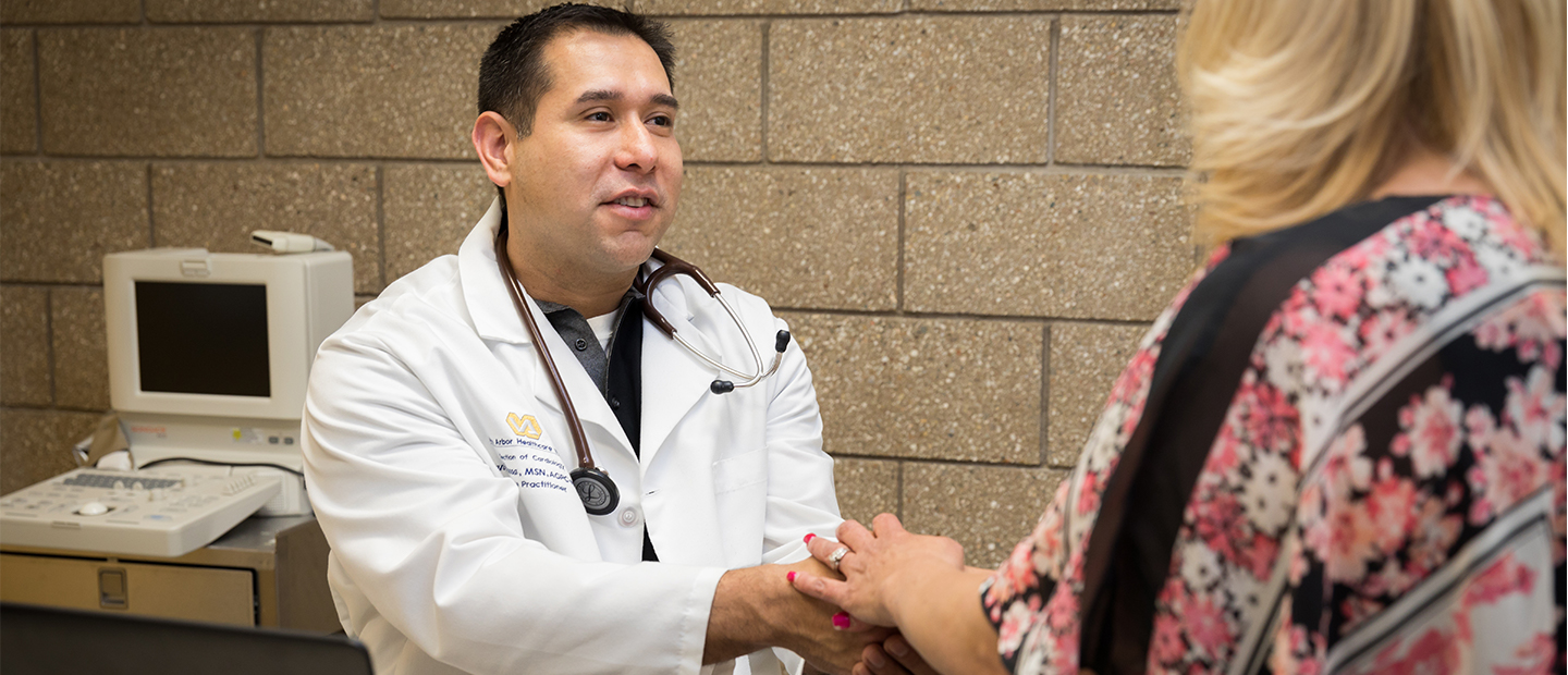 male doctor in a lab coat holding the hands of a woman who is facing him